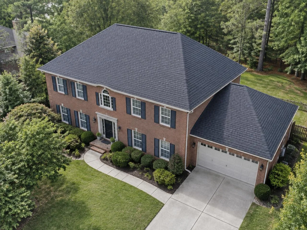 Generated aerial view of a red brick Georgia-style home with a charcoal hip roof and lower garage roof